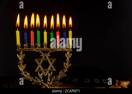 Menorah di festa ebraica con candele brucianti per Hanukkah su sfondo nero con le luci colorate delle candele. Foto Stock