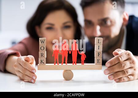 Coppia felice la protezione di equilibrio tra lavoro e vita familiare e carta ritagliata su altalena Foto Stock