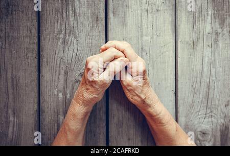 Donna anziana passa su sfondo rustico in legno. Donna anziana con le dita incrociate. Palme stropicciate allungate in avanti. Religione, prendersi cura, giorno delle madri Foto Stock