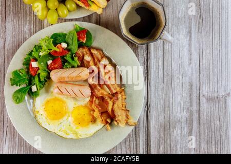 Caffè con uova fritte, pancetta, franks e insalata per colazione. Foto Stock
