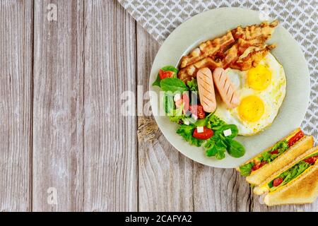 Cibo gustoso per la colazione, uova, pancetta, insalata e panini al formaggio alla griglia su un tavolo di legno. Foto Stock