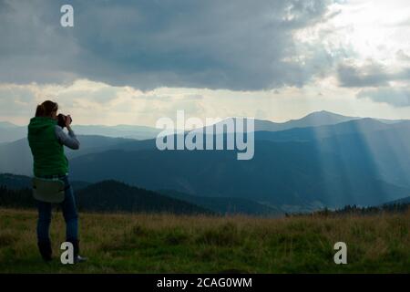 la fotografa di ragazza in montagna spara il paesaggio sul sfondo dei raggi del sole in una giornata nuvolosa Foto Stock