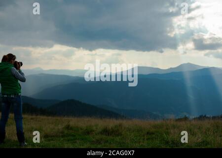 la fotografa di ragazza in montagna spara il paesaggio sul sfondo dei raggi del sole in una giornata nuvolosa Foto Stock