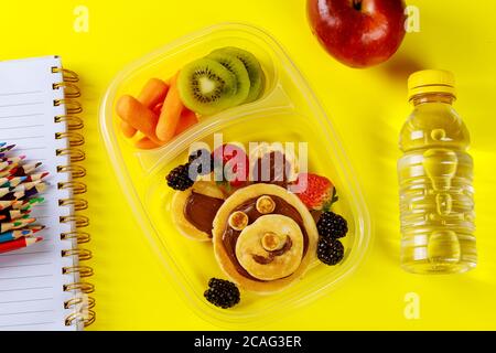 Pranzo a scuola per bambini con frittelle facciali divertenti e frutta con carote per bambini. Concetto di ritorno a scuola. Foto Stock