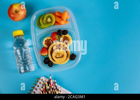 Pranzo a scuola per bambini con frittelle facciali divertenti e frutta con carote per bambini. Concetto di ritorno a scuola. Foto Stock