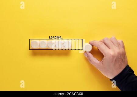 Mano che posiziona il cubo di legno per completare la barra di avanzamento del caricamento su sfondo giallo. Tempo di caricamento o concetto di processo. Foto Stock