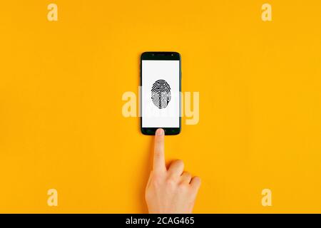Male hand pressing the smartphone button with fingerprint scan icon on the sceen. Flat lay view. Foto Stock
