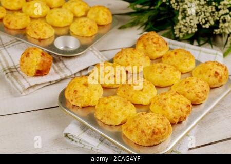 Pane al forno al formaggio brasiliano in teglia con fiori su tavola di legno. Foto Stock