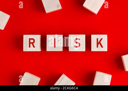 La parola rischio scritta su blocchi di legno su sfondo rosso. Concetto di gestione o valutazione del rischio. Foto Stock