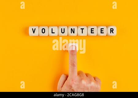 La parola volontario scritto su blocchi di legno con una mano maschio che preme il pulsante. Concetto di volontariato e di adesione a una causa. Foto Stock