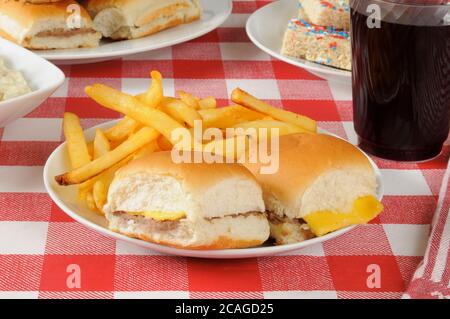 Mini cheeseburgers e patatine fritte su un tavolo da picnic caricato con cibo Foto Stock