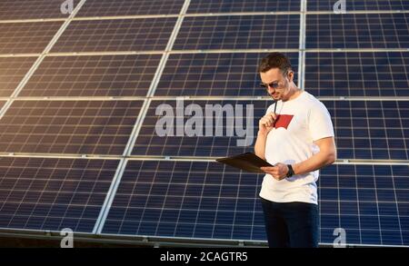 Ritratto di un giovane uomo in piedi da un pannello solare che guarda nelle sue note meditando su un certo business plan, concetto di energia verde pulita alternativa, spazio di copia Foto Stock