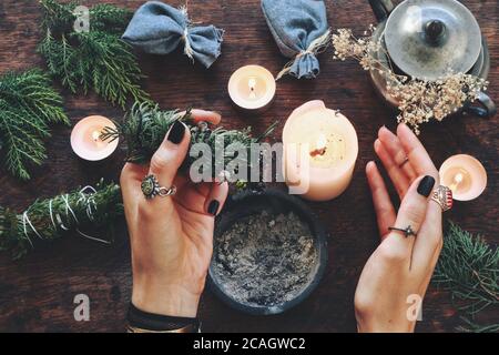 Wiccan strega tenendo il bastone di pulizia di cedro per purificare l'energia al suo altare. Donna femminile che tiene il bastone di pulizia del fumo sempreverde nelle sue mani Foto Stock