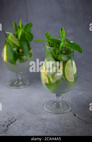 Mojito estivo con menta e calce rinfrescante cocktail con rum e ghiaccio in vetro su sfondo grigio. Cocktail mojito su tavolo in pietra. Vetro glassy alto per bevande Foto Stock