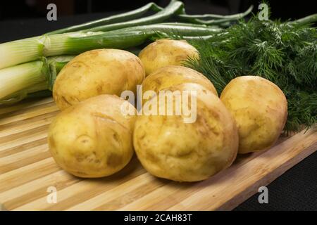 Patate giovani, ravanello, cipolle verdi, aneto su tavola di legno, fondo nero Foto Stock