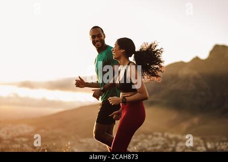 Vista laterale di uomo fitness e donna che corrono insieme al mattino. Una coppia in forma fisica che si gode la loro corsa mattutina su una collina. Foto Stock