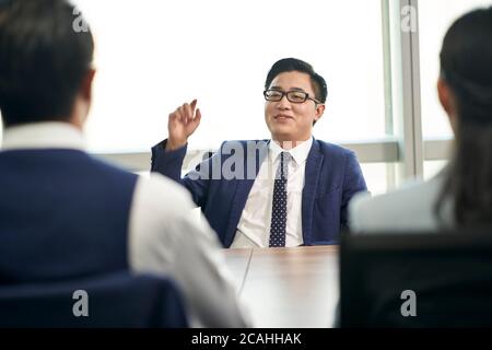 giovane uomo d'affari asiatico che parla grande davanti agli intervistatori di ore durante l'intervista di lavoro Foto Stock