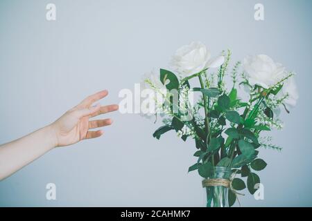 Persona che raggiunge per il bouquet splendidamente organizzato di fiori contro una parete bianca Foto Stock