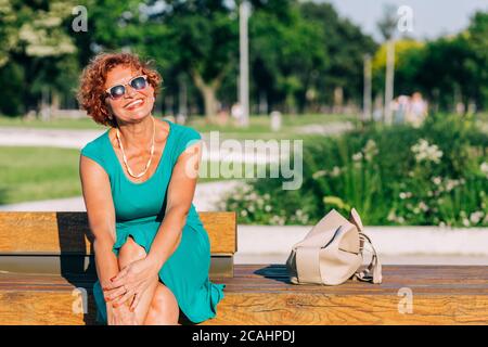 Donna matura seduta sulla panchina nel parco in estate Foto Stock