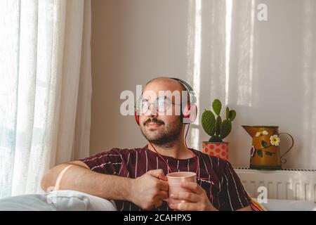 i giovani si stanno bene a casa, ascoltando musica, bevendo caffè e tè. Un adolescente a riposo che corre con un tablet e il Leptop in mano. Foto Stock