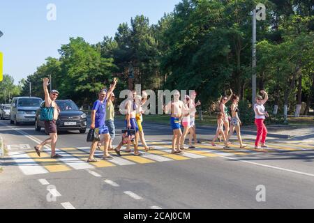 Anapa, Russia - 3 luglio 2020: Un gruppo di turisti allegri pedoni attraversano la corsia pedonale sorridendo e sventolando le mani Foto Stock