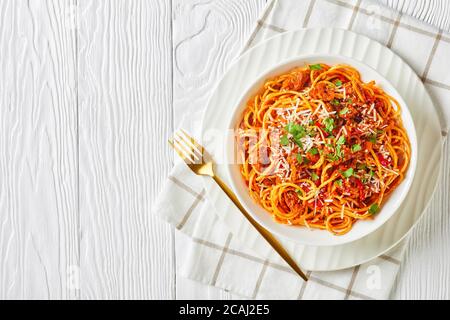 spaghetti con salsicce di maiale ragù, pomodori, verdure, spezie cosparse di parmigiano grattugiato e prezzemolo tritato in una ciotola bianca, vista da Foto Stock