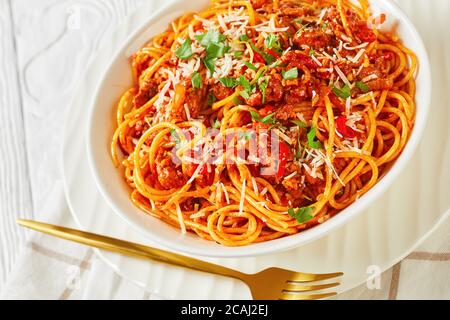 spaghetti con salsicce di maiale ragù, pomodori spezie cosparse di parmigiano grattugiato e prezzemolo tritato in una ciotola bianca, vista dall'alto, Foto Stock