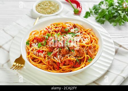 spaghetti con salsicce di maiale ragù, pomodori spezie cosparse di parmigiano grattugiato e prezzemolo tritato in una ciotola bianca, vista dall'alto, clo Foto Stock