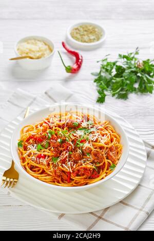 spaghetti con salsicce di maiale ragù, pomodori spezie cosparse di parmigiano grattugiato e prezzemolo tritato in una ciotola bianca, vista verticale da a. Foto Stock