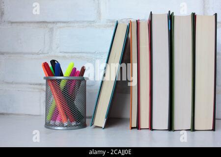 Pila di libri e pennarelli sul tavolo contro muro di mattoni bianchi. Ritorno a scuola. Spazio di copia Foto Stock