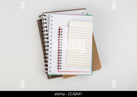 una pila di diversi quaderni a spirale si trova su un tavolo bianco con una matita, concetto di ufficio Foto Stock