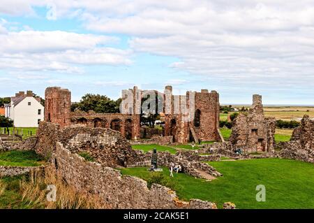 Le vaste rovine del Priorato di Lindisfarne che contiene la chiesa priorale medievale con le sue alte torri, arco arcobaleno e resti di edifici in pietra Foto Stock