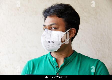 Adulto indiano maschio che indossa un respiratore bianco N95 in verde T-Shirt guardando la fotocamera con la testa rivolta a 45 gradi con sfondo testurizzato Foto Stock