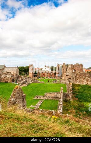 Le vaste rovine del Priorato di Lindisfarne che contiene la chiesa priorale medievale con le sue alte torri, arco arcobaleno e resti di edifici in pietra Foto Stock