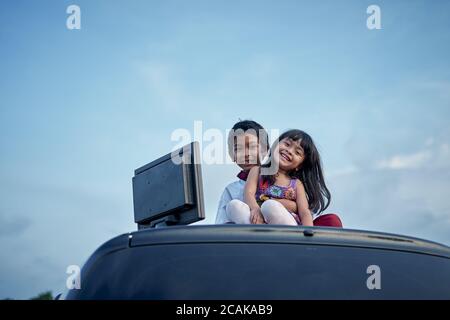 Ragazzo e ragazza che fanno i compiti usando il computer sulla parte superiore del tetto dell'automobile, nuovo concetto di istruzione normale Foto Stock