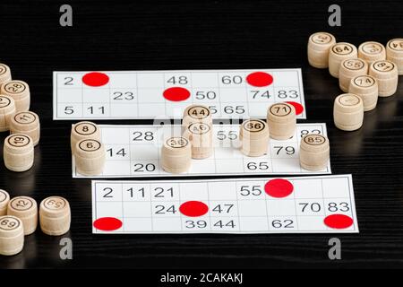 Botti di lotto, carte e patatine di legno per giocare su un tavolo nero. Foto Stock