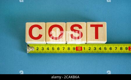 Parola 'costo' sui cubi disposti dietro il righello su sfondo blu bello. Concetto. Foto Stock