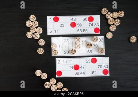 Botti di lotto, carte e patatine di legno per giocare su un tavolo nero. Foto Stock