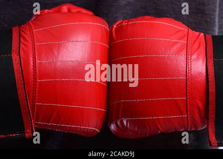 Boxer preme le mani insieme. Gli atleti si mettono in guanti di pelle per scatola su sfondo grigio, primo piano. Concetto di sport e competizione. L'uomo indossa guanti di boxe rossi. Foto Stock