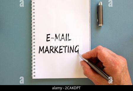 La mano maschile scrive 'e-mail marketing' su nota bianca, isolato su sfondo blu. Foto Stock