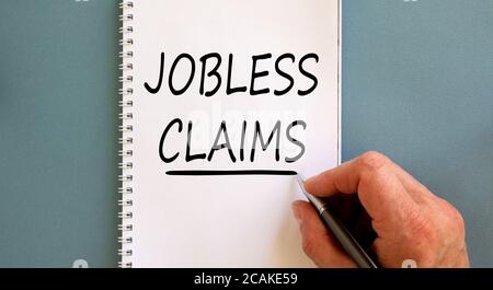 La mano maschile scrive 'jobless claims' su nota bianca, isolata su sfondo blu. Concetto aziendale. Foto Stock