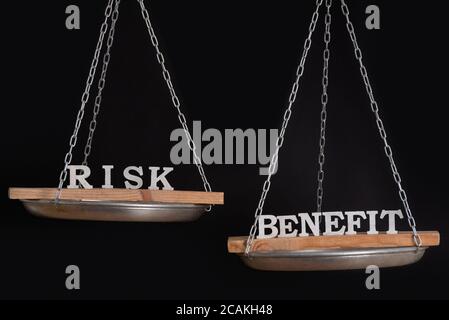Parole rischio e beneficio in equilibrio. Concetto di equilibrio. Scala su sfondo nero. Foto Stock