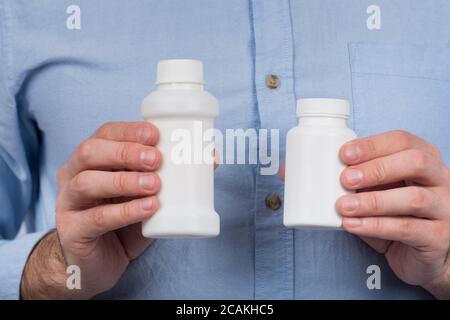 Due bottiglie di plastica bianche per medicinali o vitamine in mani maschili. Spazio di copia. Simulazione. Foto Stock