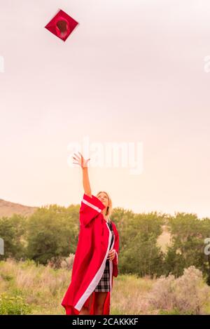 Bella ragazza giovane gettando cappello rosso di graduazione in aria festeggiando. Foto Stock