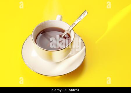 Il sole del mattino splende per una tazza di porcellana bianca appena prodotta tè su tavola gialla Foto Stock