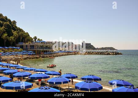 Vista panoramica sulla baia con file di ombrelloni sulla spiaggia sabbiosa e sull'antico borgo peschereccio di Lerici sullo sfondo in estate, Liguria, Italia Foto Stock
