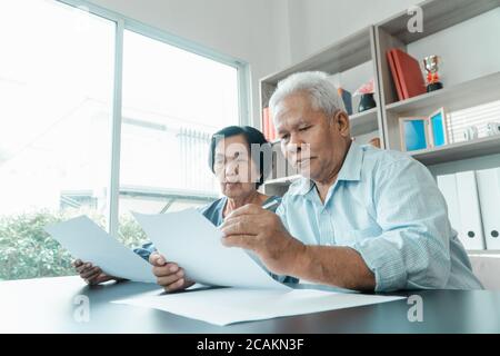 Coppia asiatica senior che utilizza la calcolatrice e la documentazione sulla scrivania a casa per calcolare le spese e il reddito. E risparmio dopo il pensionamento. Concetto di fina Foto Stock