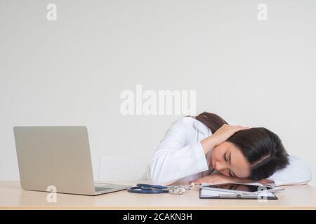 Giovane donna asiatica dottore seduto sulla scrivania, lei sembra infelice e stanca a causa di lavoro eccessivo, concetto di stressato e responsabilità medico, trattare Foto Stock
