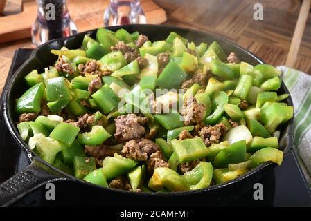 Manzo macinato stagionato e peperoni verdi a dadini che bollono in un padella in ghisa Foto Stock