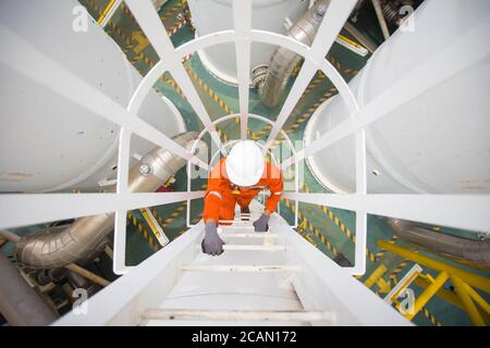 Il tecnico di processo sale fino alla cima della disidratazione del gas serbatoio per ispezionare e controllare le condizioni anomale del processo in la processina centrale di petrolio e gas Foto Stock